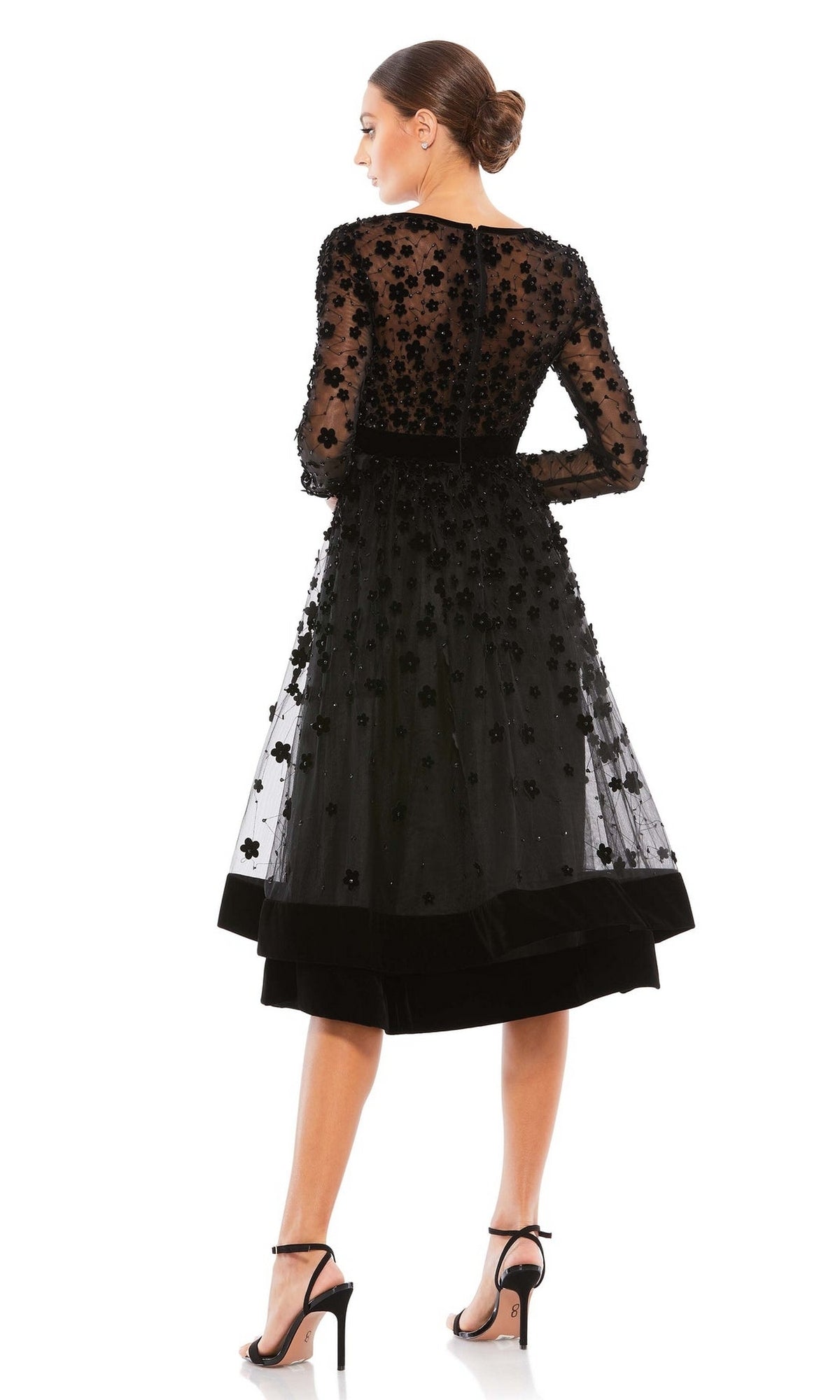 Woman viewed from the back in the Mac Duggal 67007 knee-length wedding-guest dress, featuring long sleeves, black sheer overlay, floral embellishments, and paired with black high-heeled sandals.